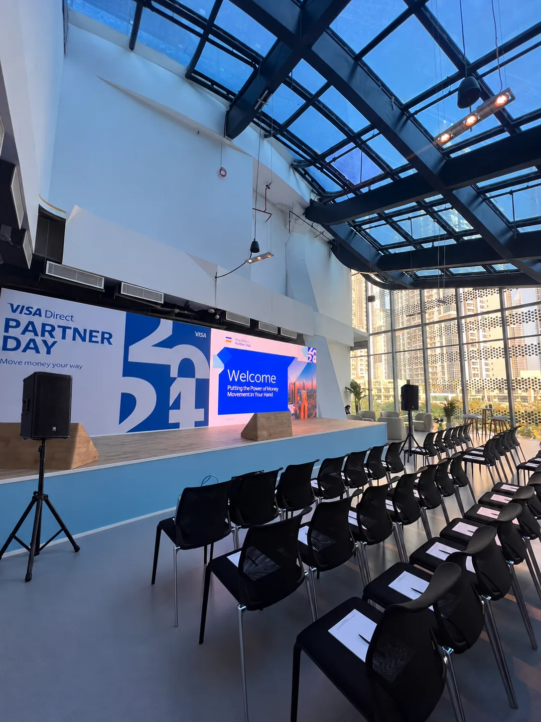 Illustrative corporate presentation stage with PA speakers on tripod stands facing the audience