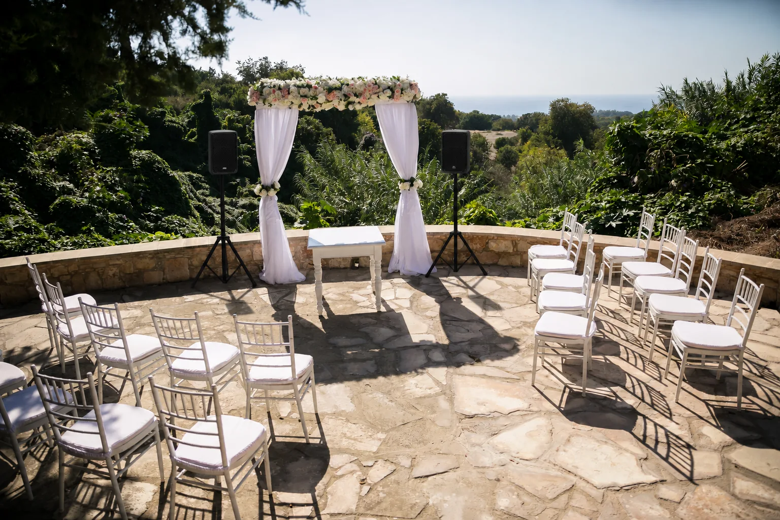 Illustrative seaside wedding PA setup with two speakers on tripods beside a floral arch